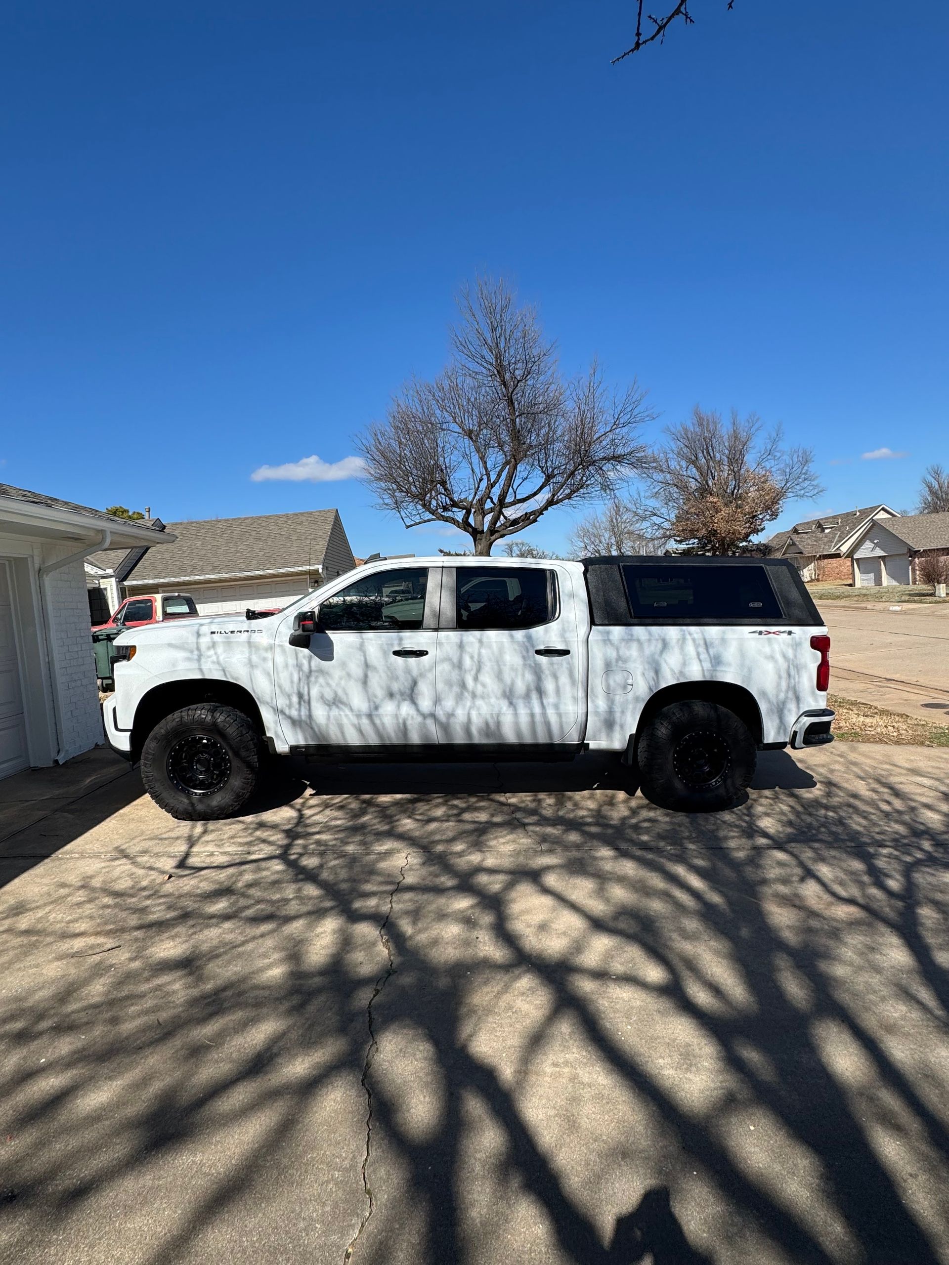 White pickup truck parked in a driveway under a clear blue sky, with tree shadows on the pavement