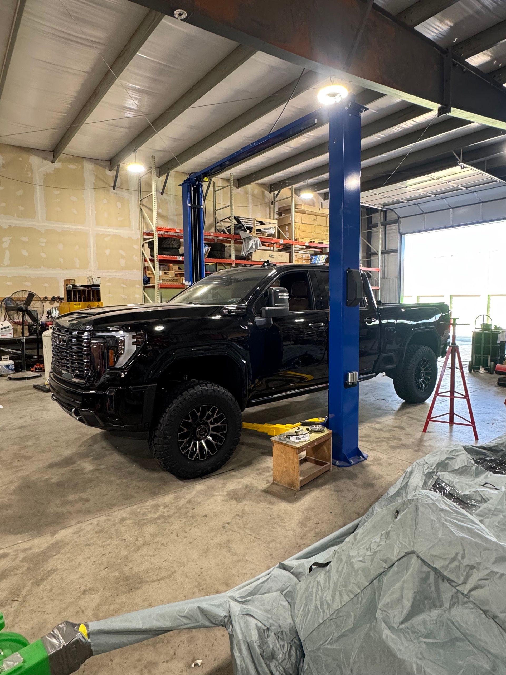 Black pickup truck in an auto shop lift bay with tools and shelving in the background