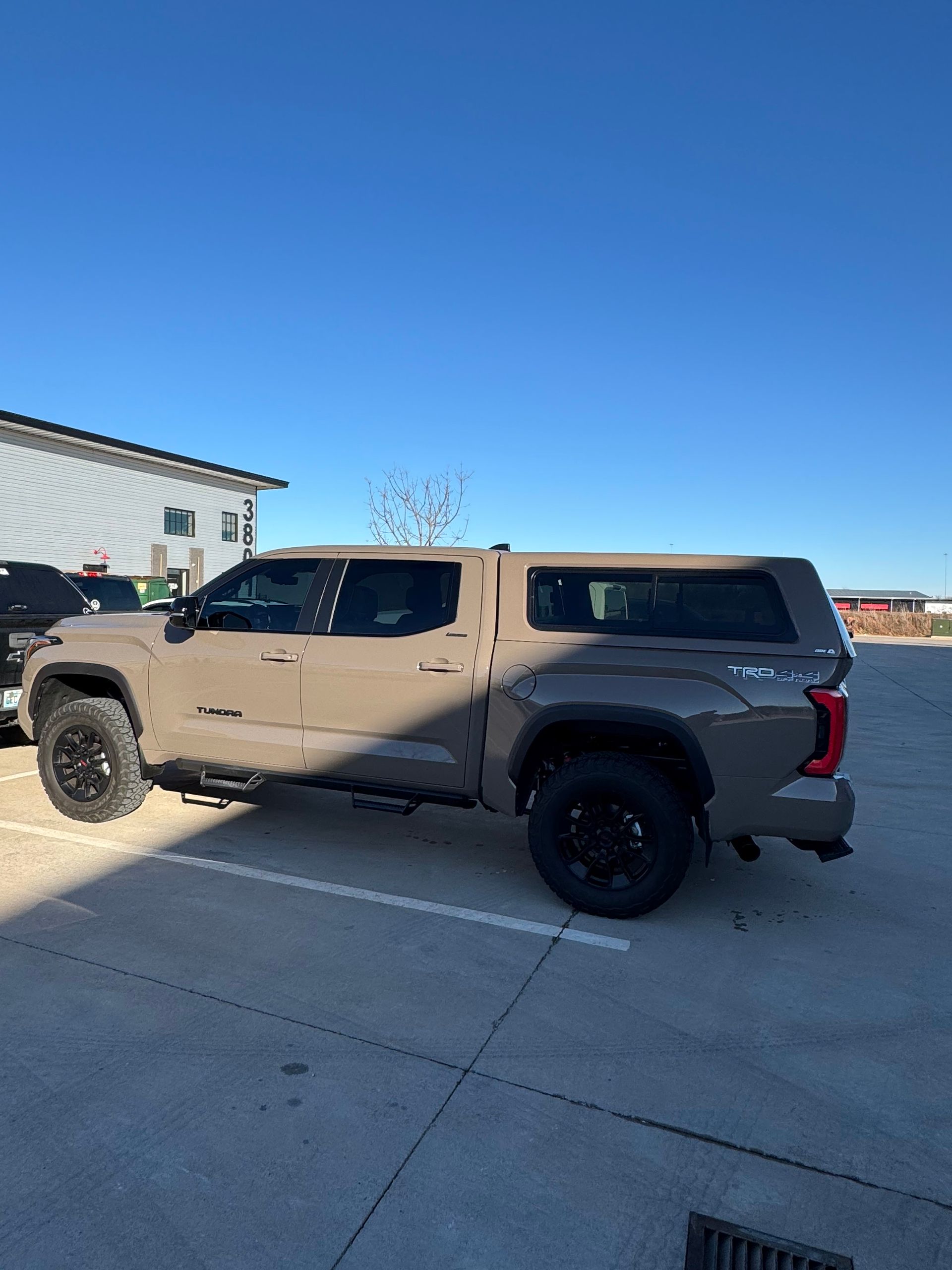 Tan pickup truck parked on a sunny lot beside a building under a clear blue sky