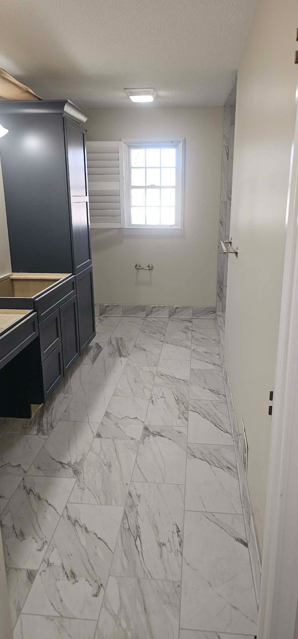 A bathroom with marble tile floors and dark cabinets, a window in the back, and a door on the right.