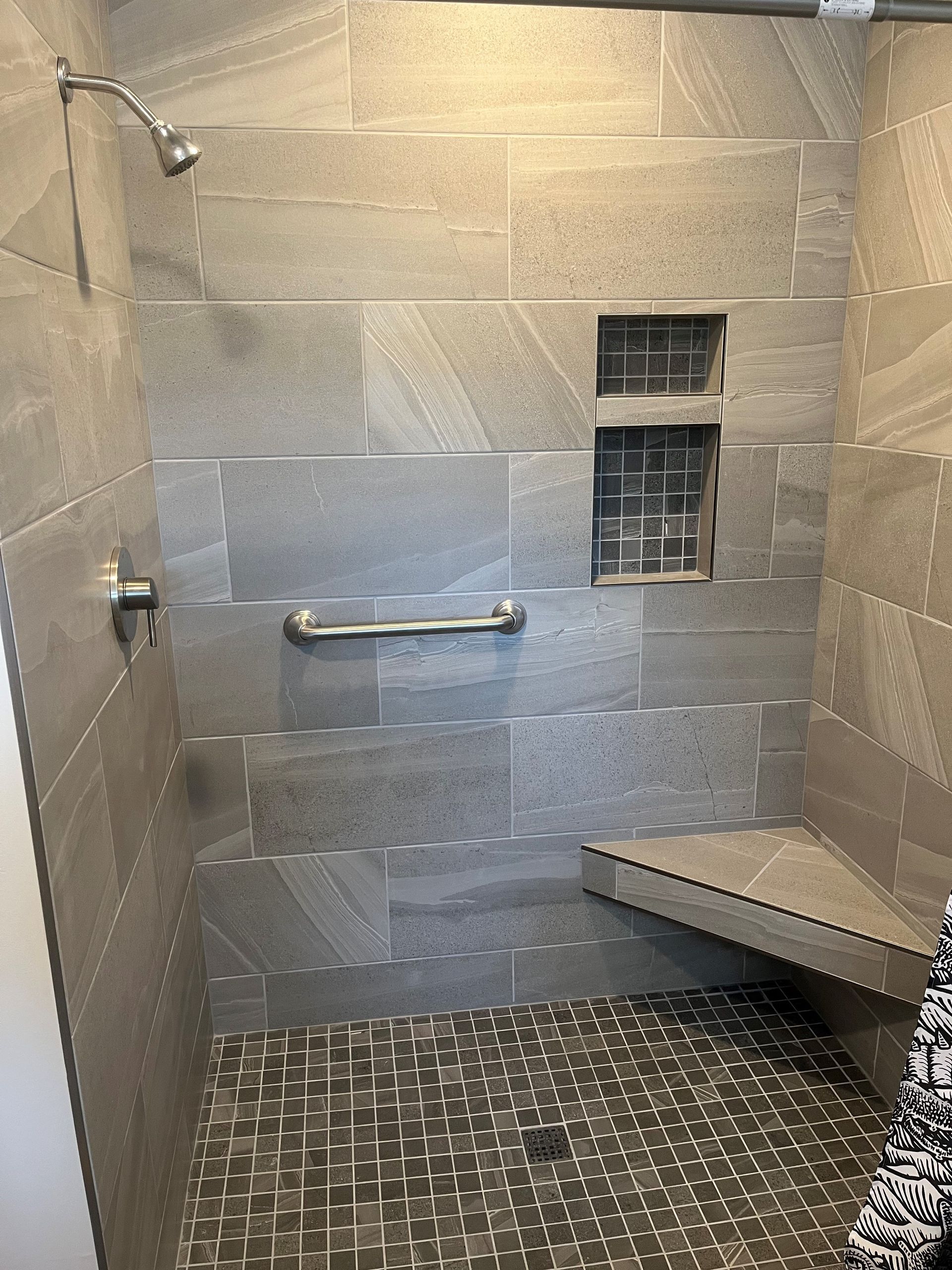 A walk in shower with a bench and a hand rail.