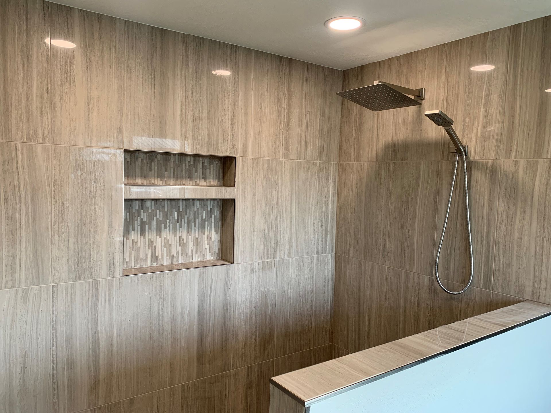A shower with a built in shelf and a shower head.