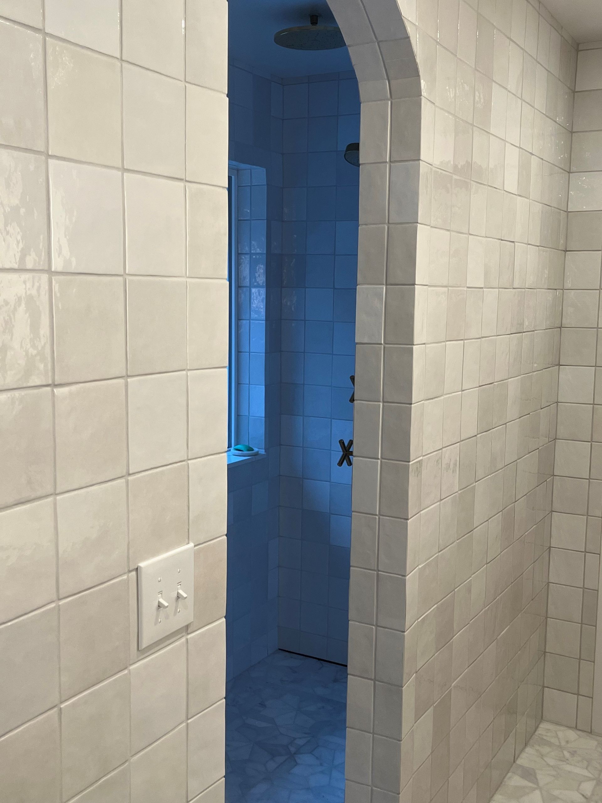 A bathroom with white tiles and a door leading to a shower.
