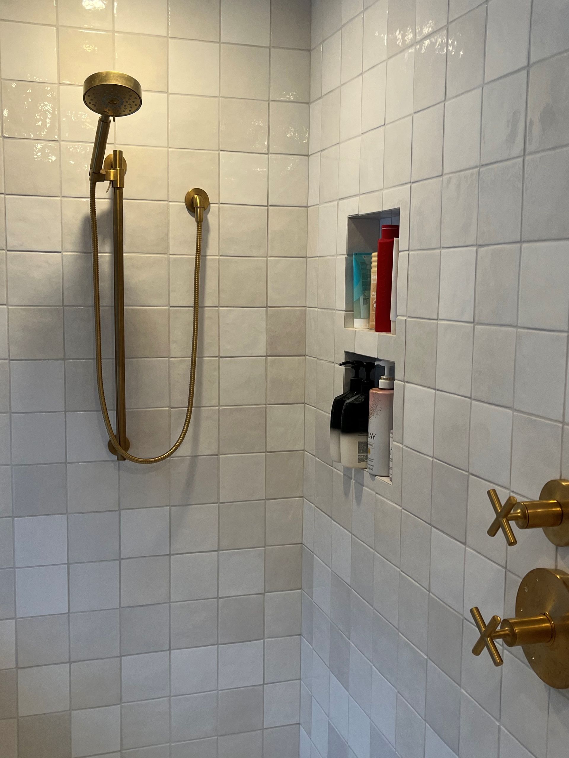 A shower with white tiles and gold shower head and faucets.