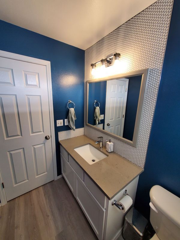A bathroom with blue walls , a sink , a toilet and a mirror.