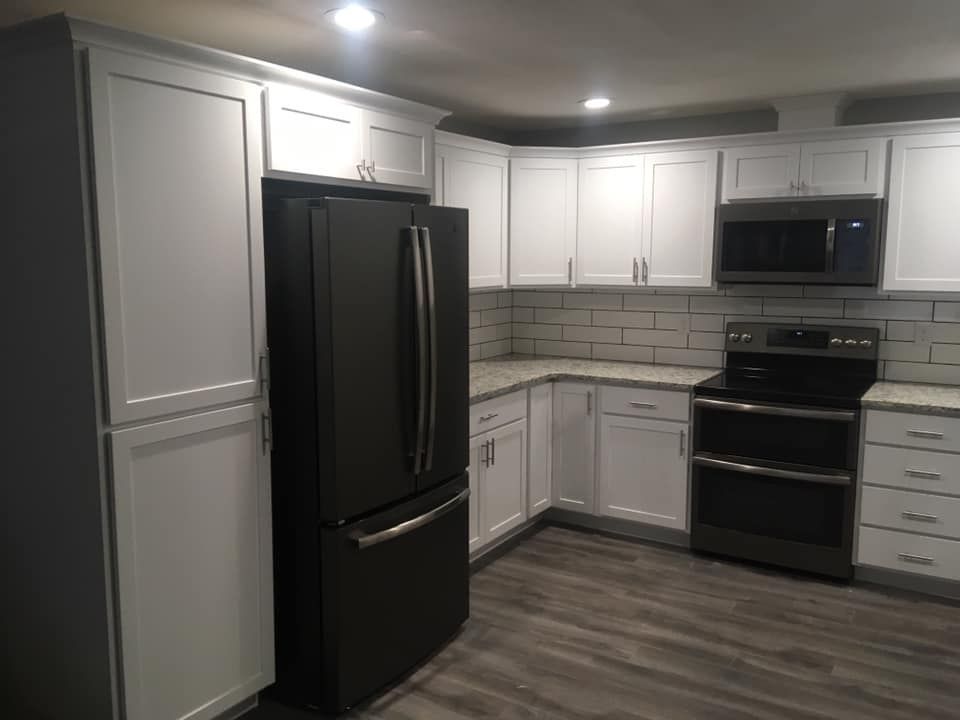 A kitchen with white cabinets , a black refrigerator , a stove , and a microwave.