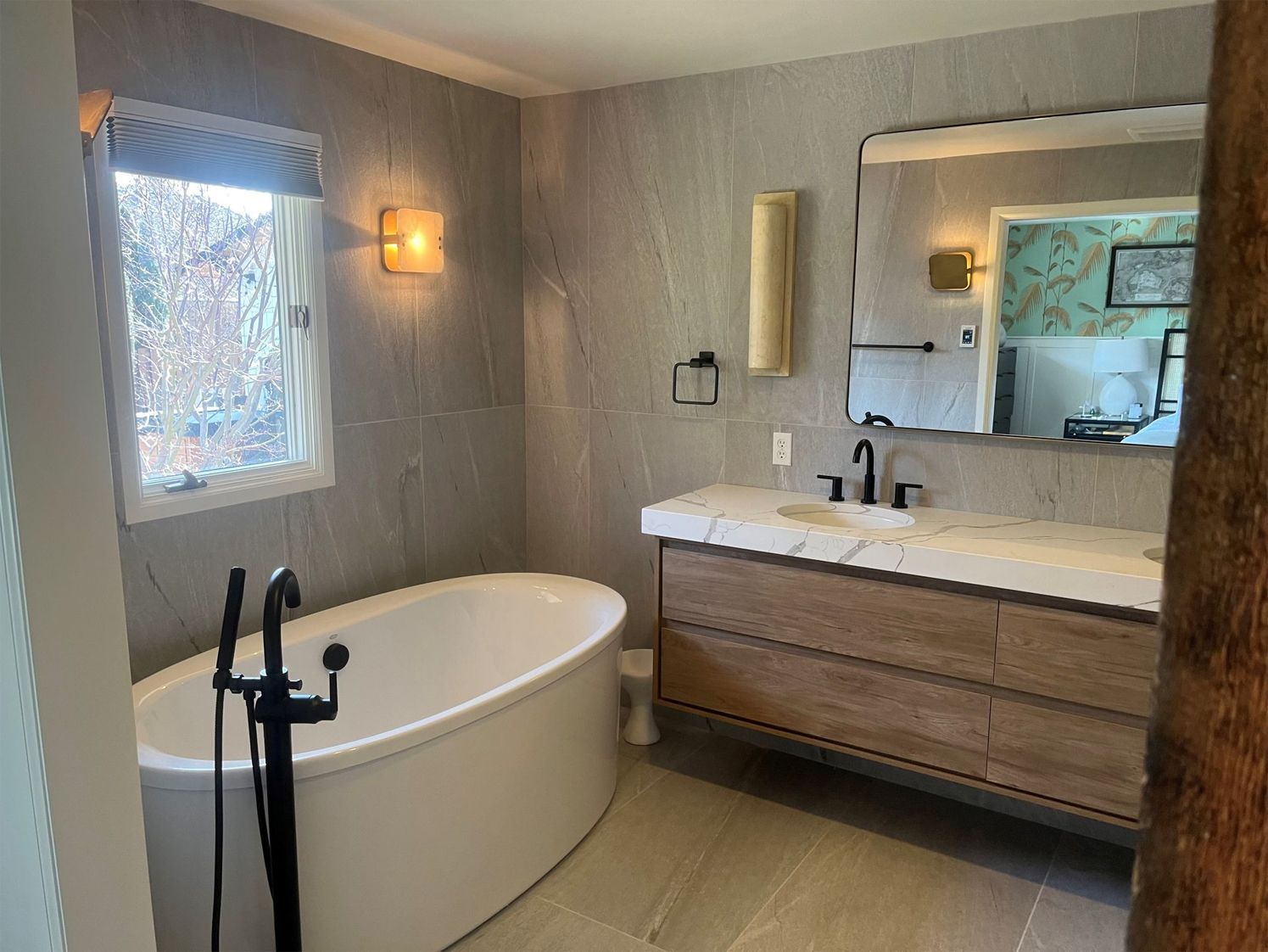 A bathroom with a tub, sink, mirror and window.
