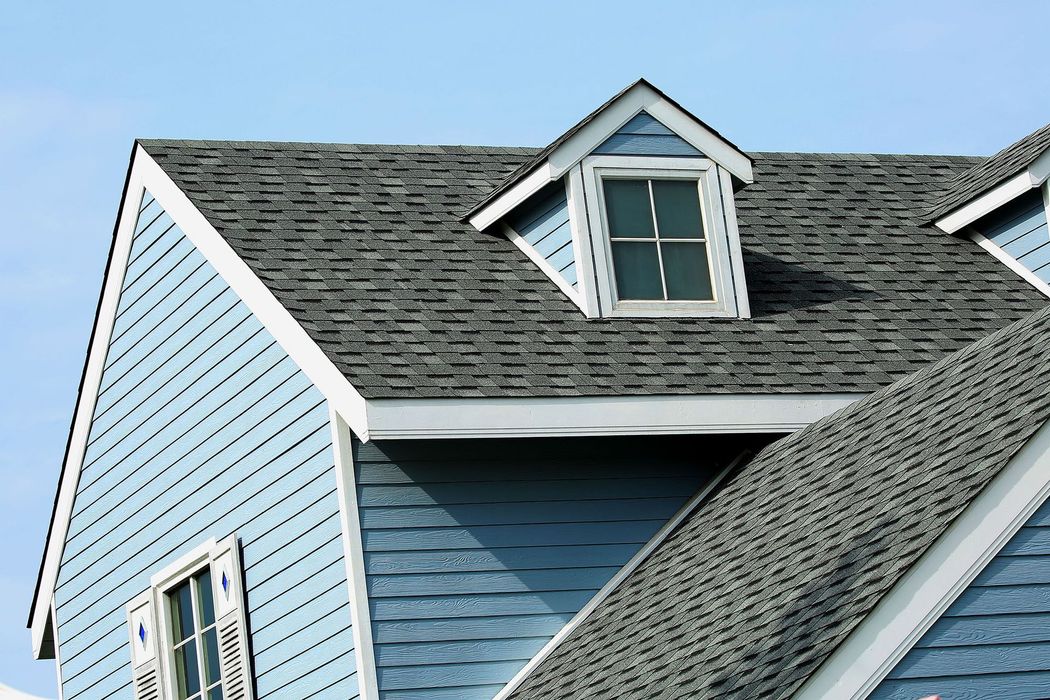 Blue house roof with gray shingles and a dormer window against a clear sky