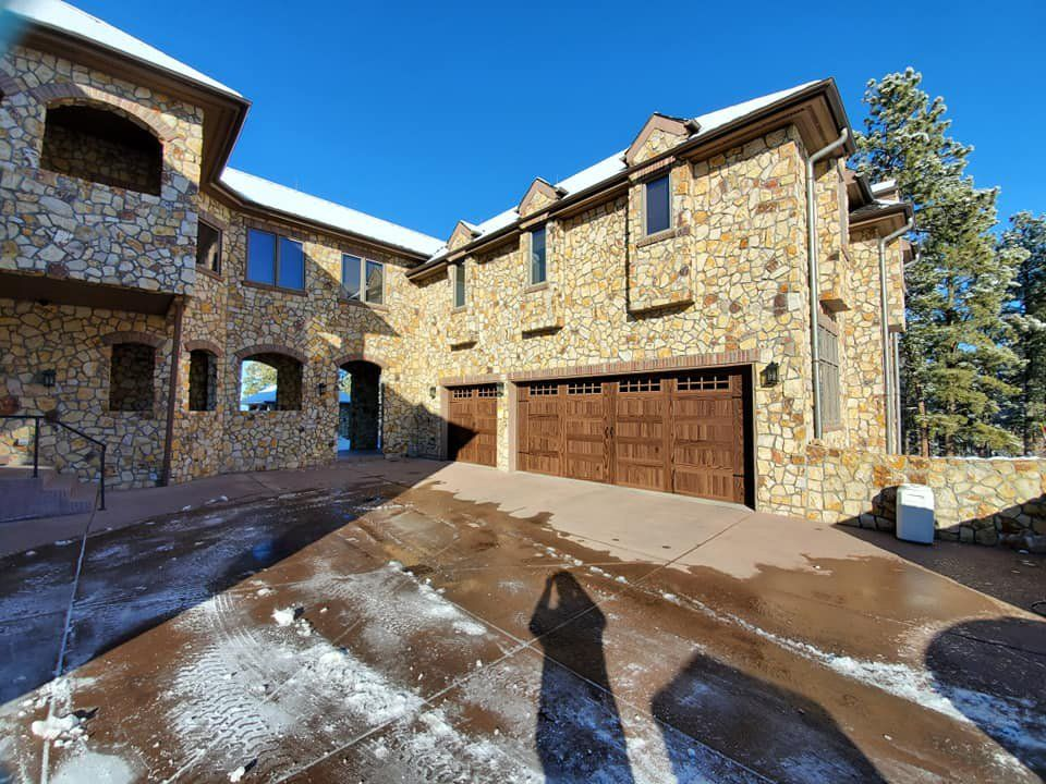 A large stone house with a brown garage door and a snowy driveway.