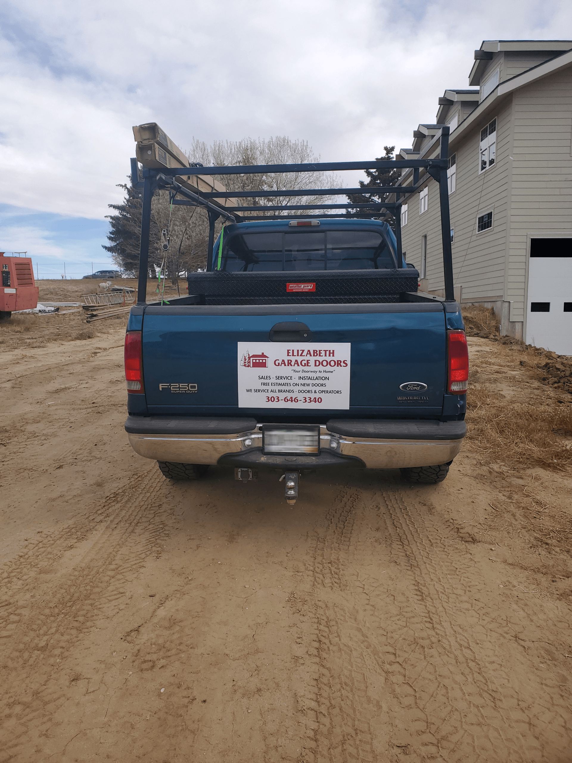 A blue truck is parked in a dirt lot in front of a house.