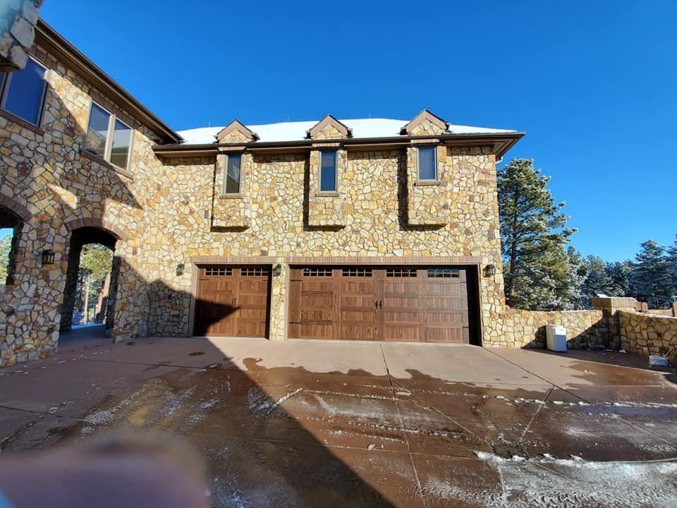 A large stone house with three garage doors and a driveway.