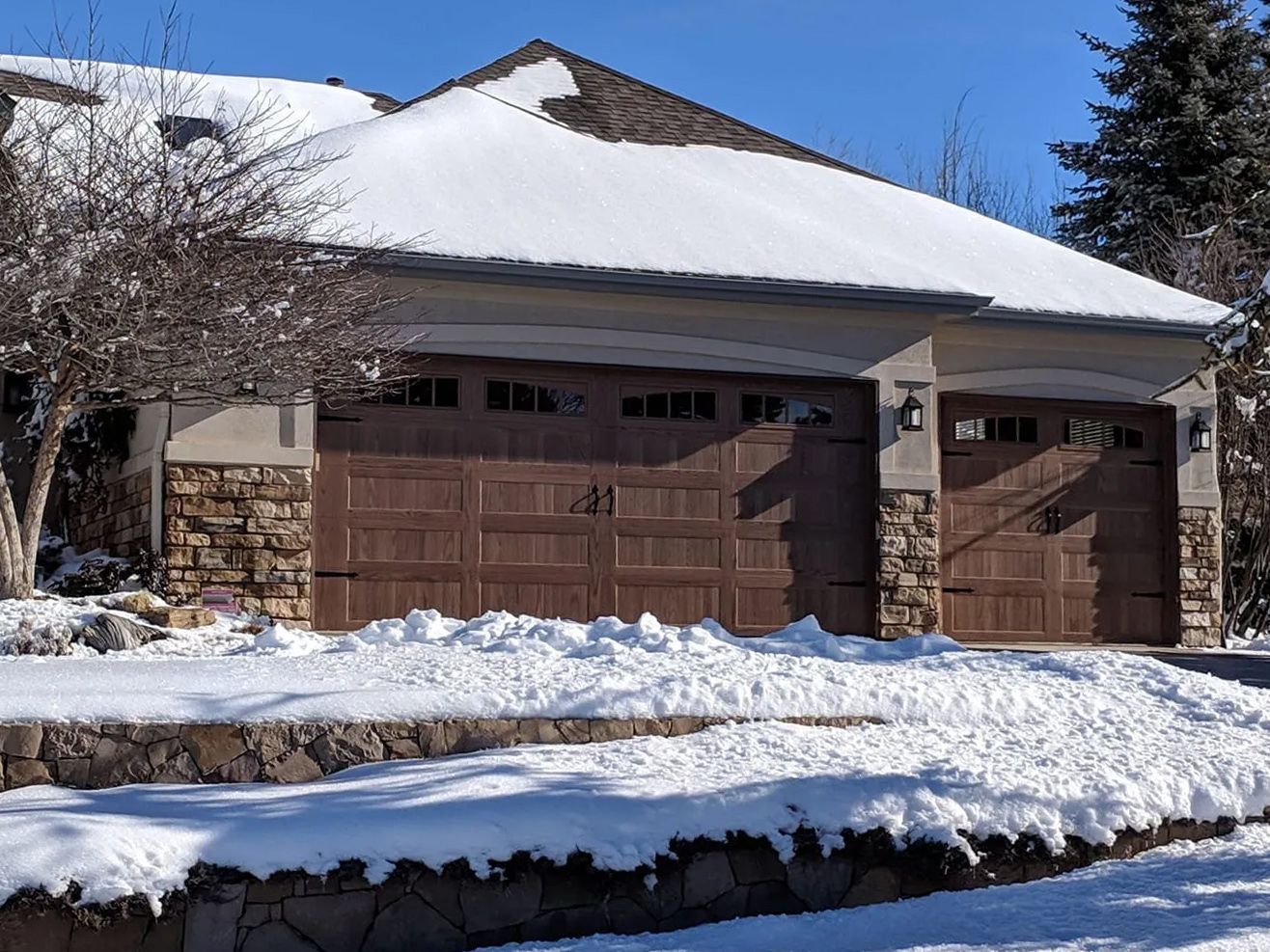 A house with three garage doors is covered in snow.