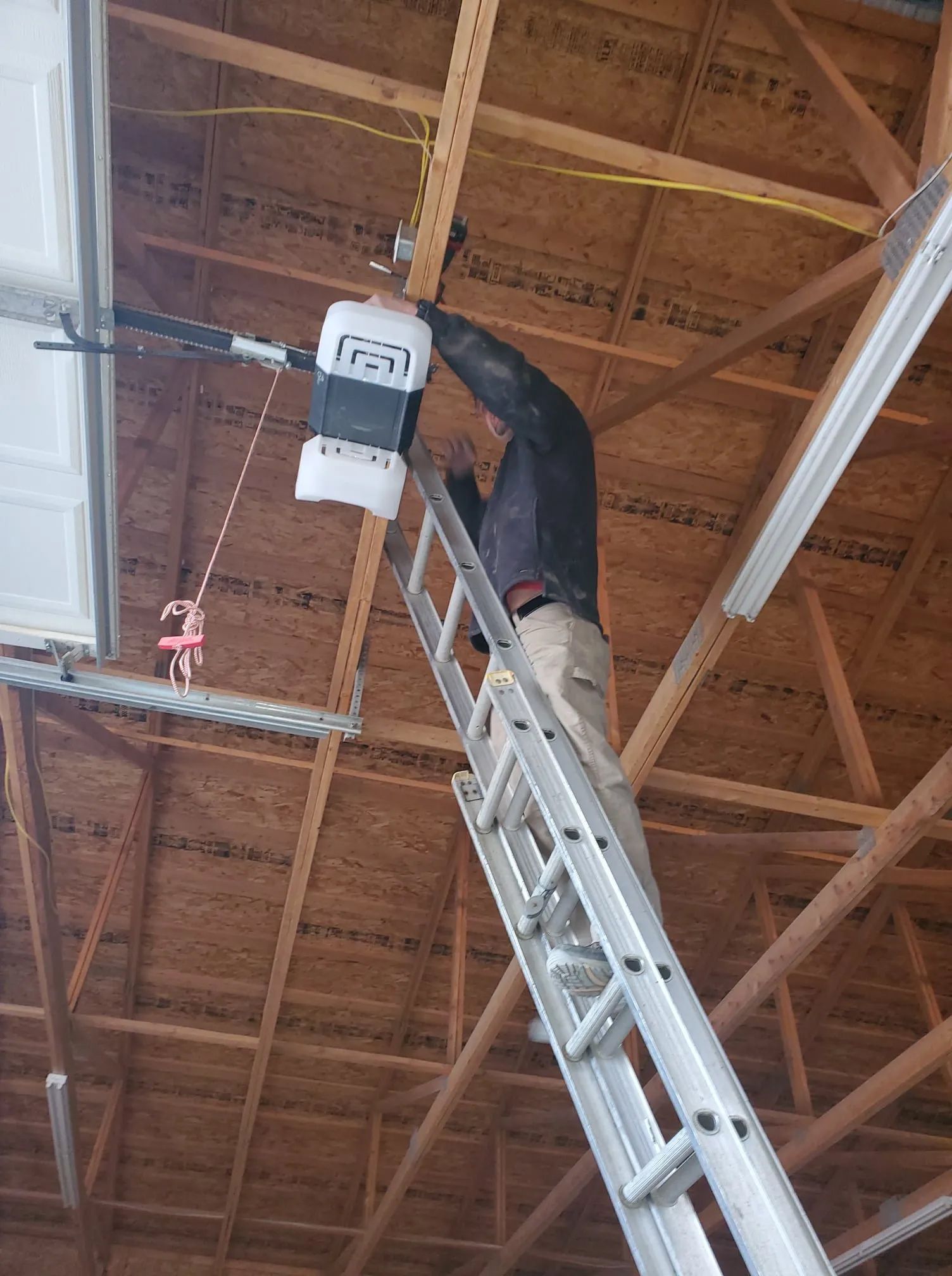 A man is standing on a ladder fixing a garage door opener.