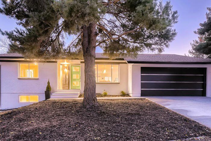 A white house with a black garage door and a tree in front of it