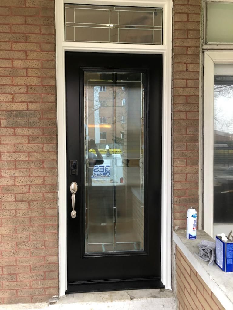A black door with a glass window is on a brick building.