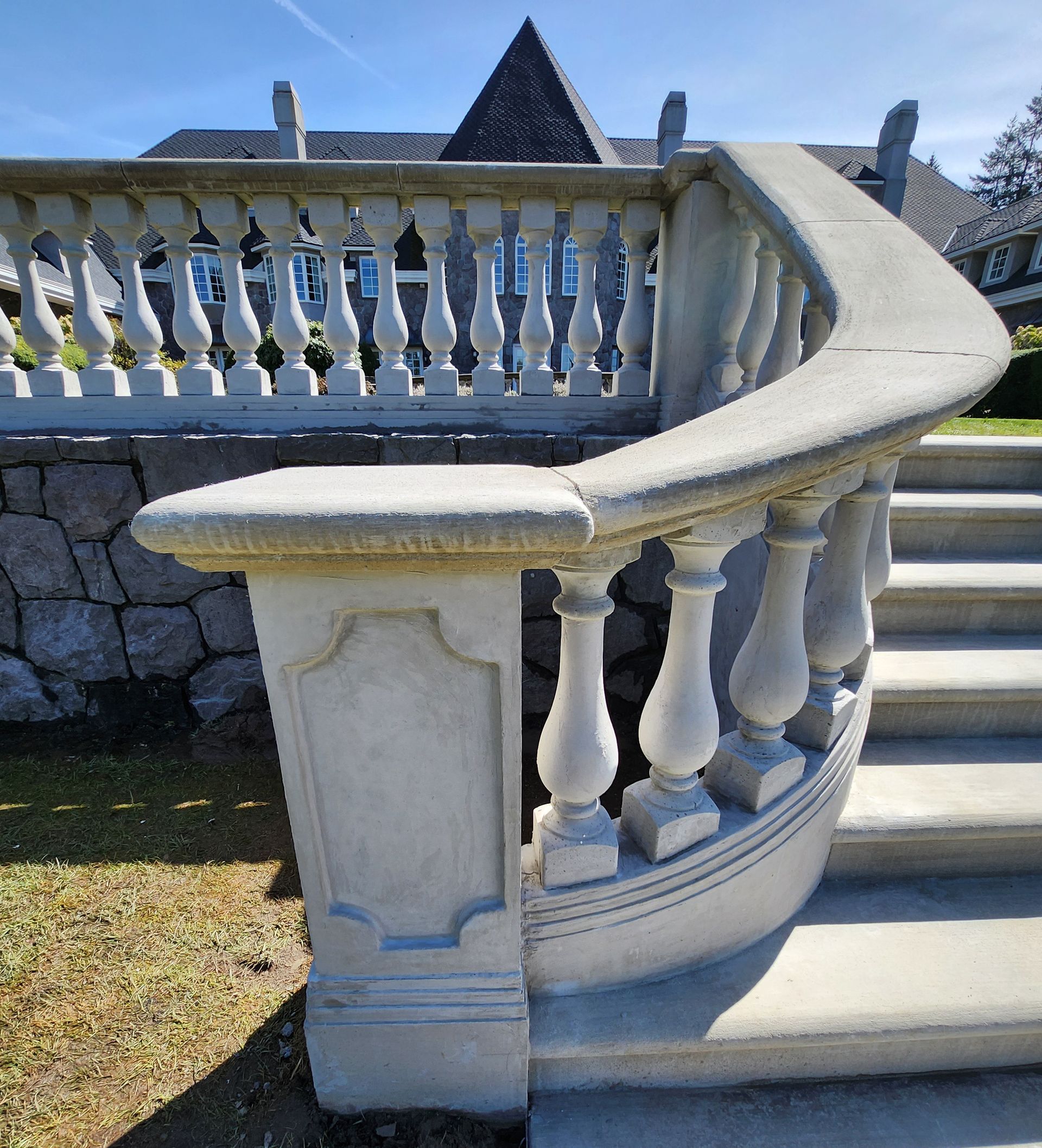 Curved stone staircase with balustrade. Gray steps, white pillars, and a stone wall in a sunny outdoor setting.