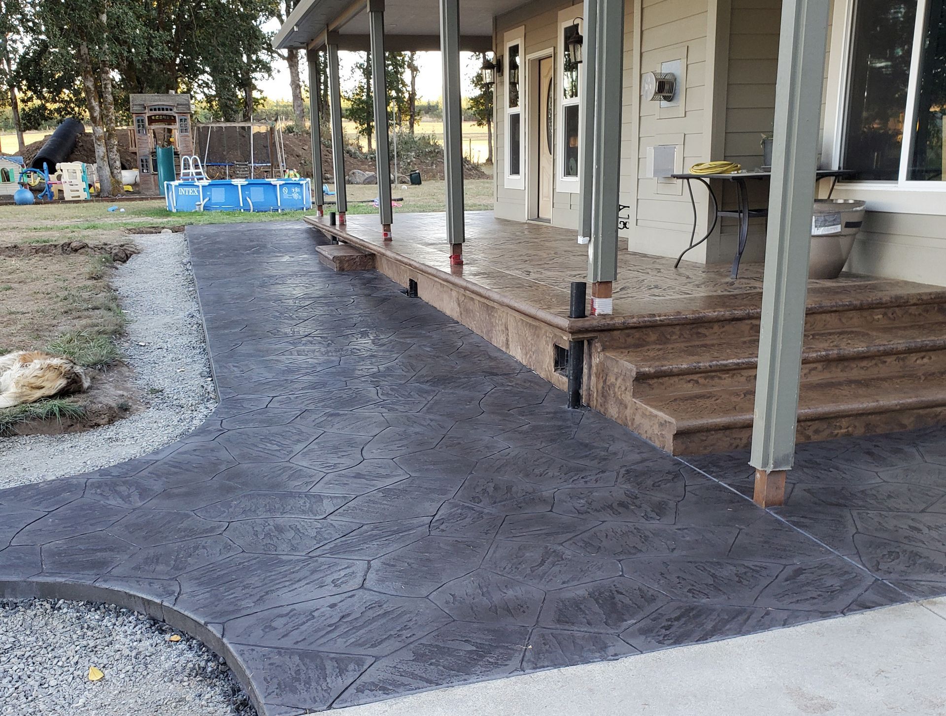 Dark gray stamped concrete pathway and porch with steps leading to a house.
