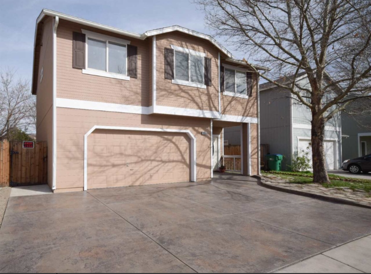 Two-story beige house with a driveway and garage, a tree, and a neighboring house.