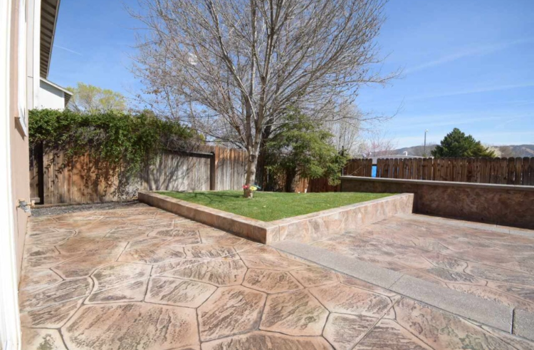 Backyard with patterned concrete patio, small grass area, and a tree against a wooden fence.