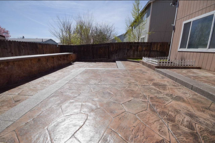 Stamped concrete patio with a decorative border, in a backyard setting.