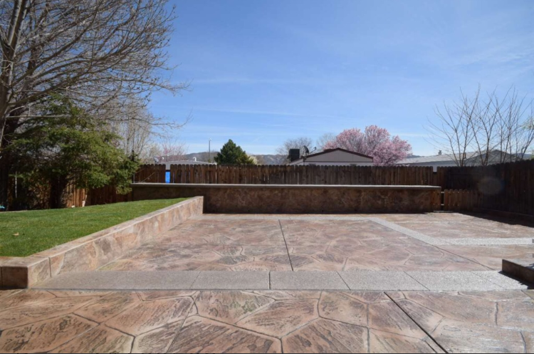 Backyard patio with stamped concrete, a grassy area, and a wooden fence under a blue sky.