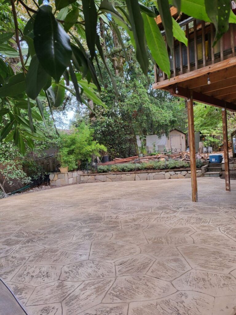 Stamped concrete patio in a backyard setting with trees and a wooden overhang.