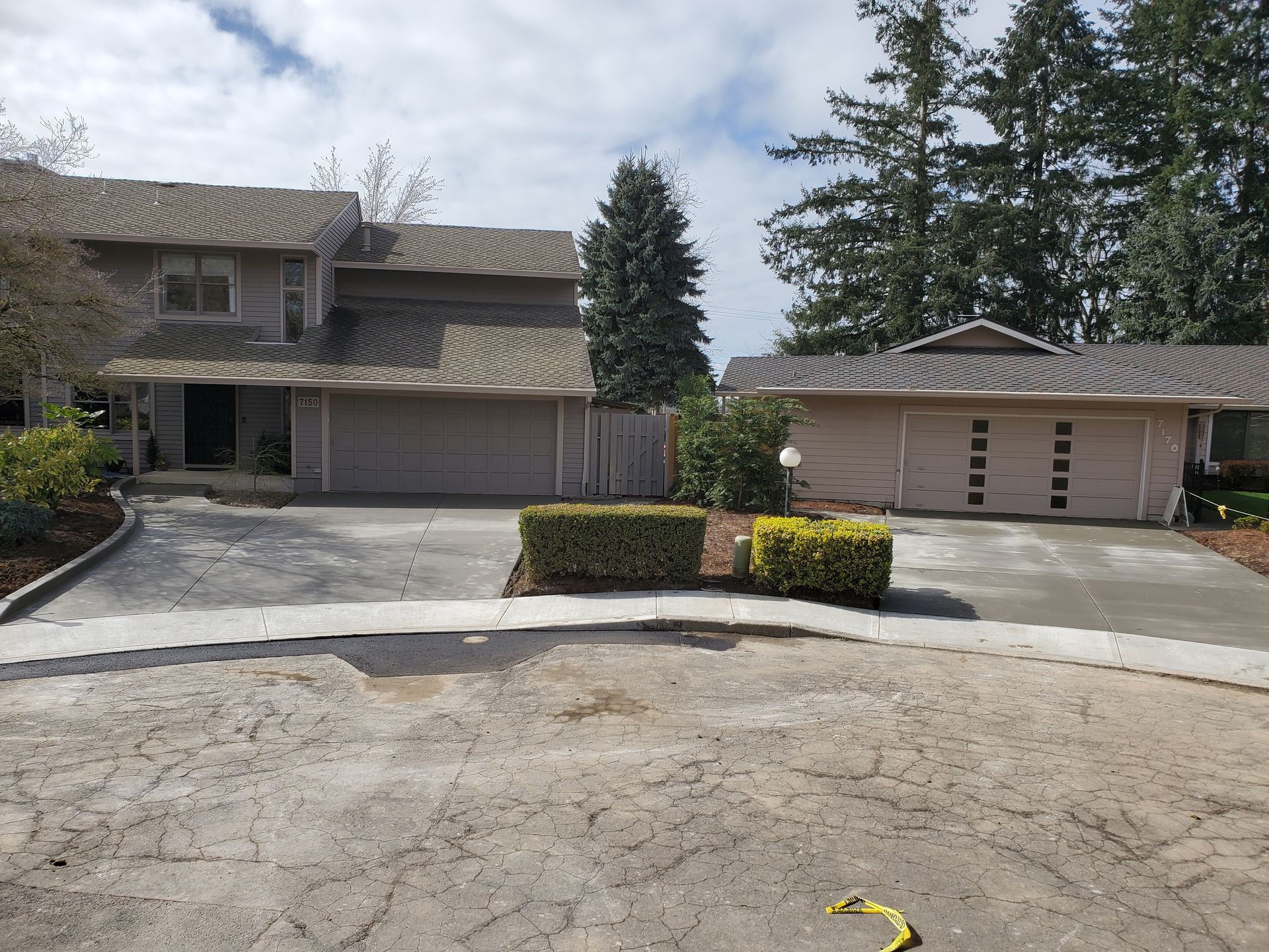 Two-story beige homes with attached garages, shrubs, and cracked pavement in front.