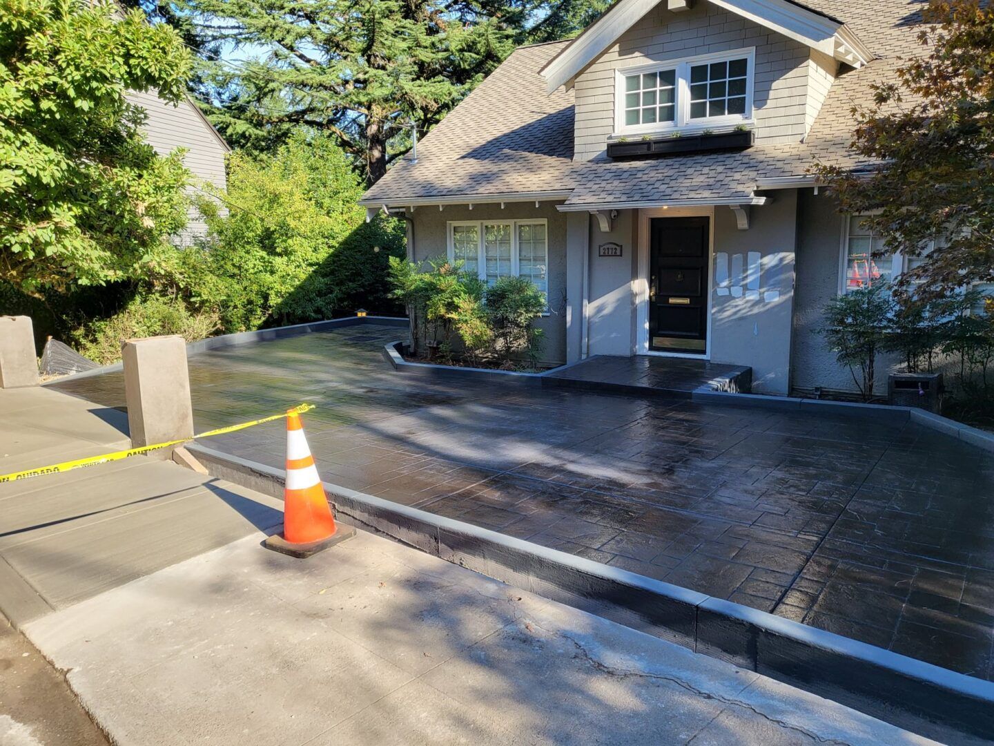 Freshly poured concrete driveway in front of a house, with orange safety cone and caution tape.