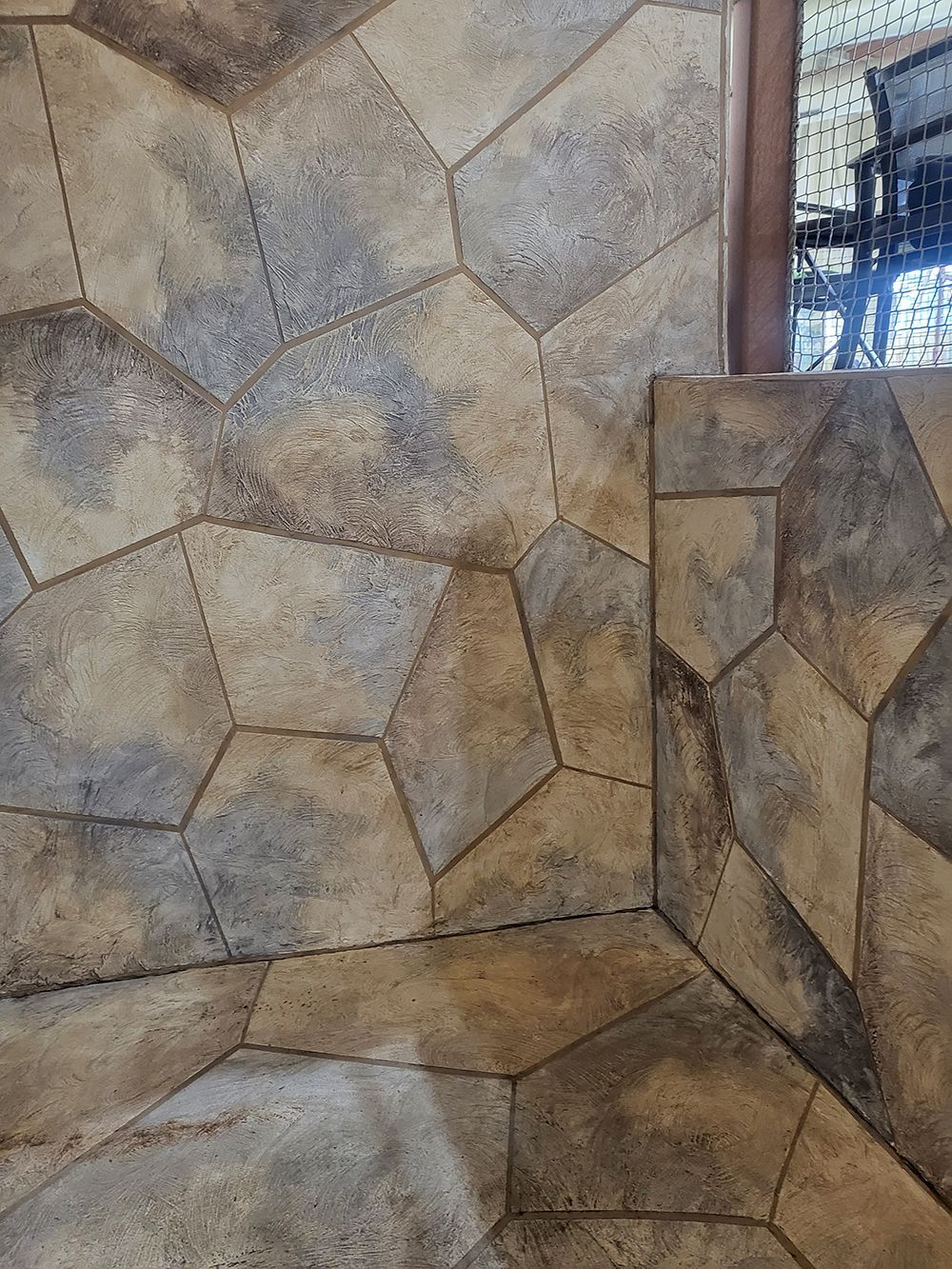 Stone-like wall and floor tiles in neutral tones, corner of a room, partial view.
