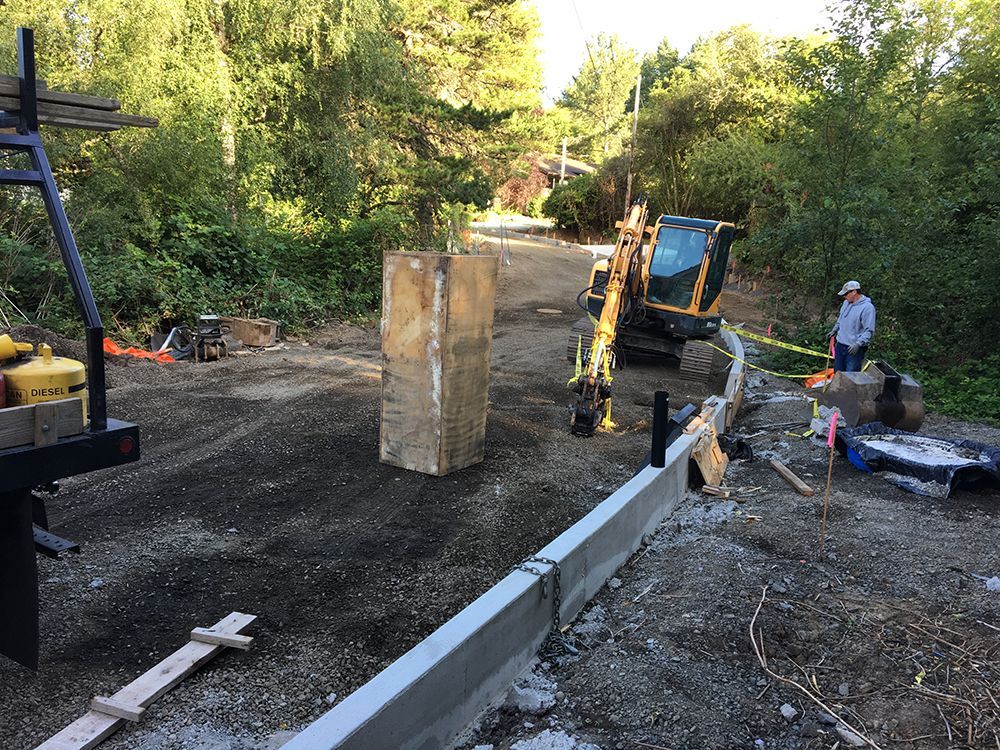 Construction site with concrete barrier, excavator, and person standing nearby.