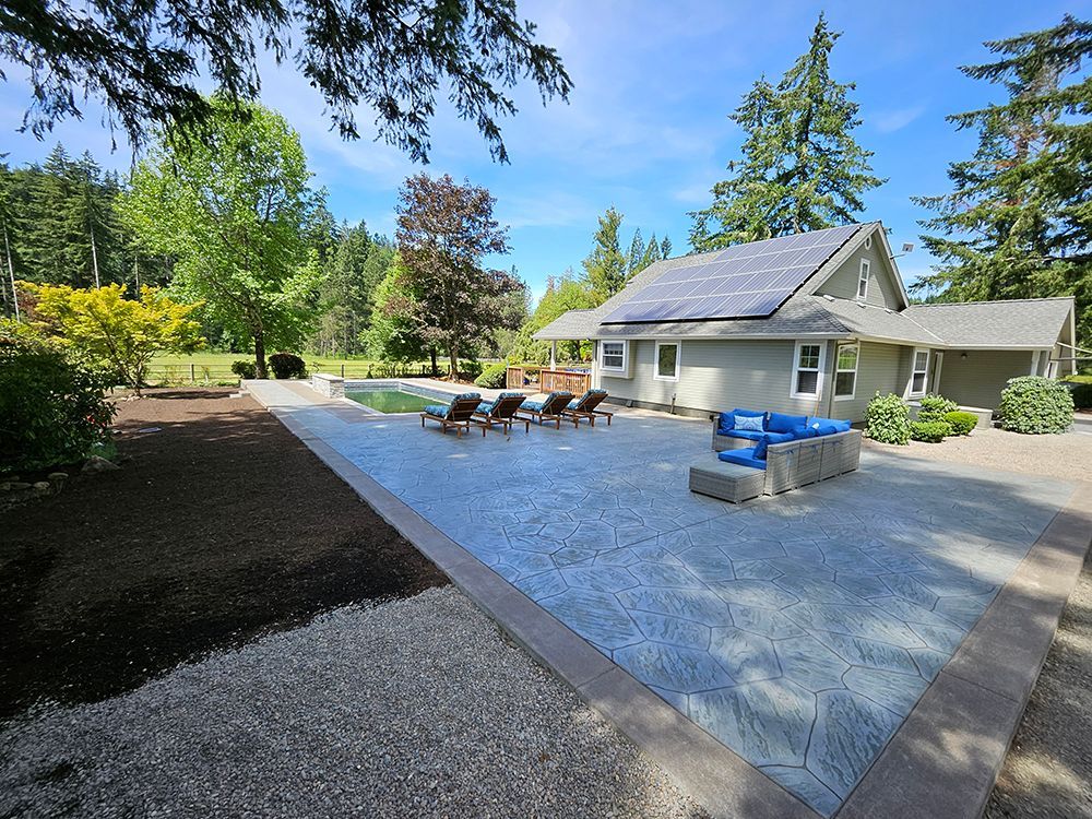 Backyard with pool, patio, and house. Blue sky, green trees, and lounge chairs.
