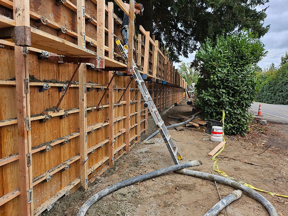 Construction site with wooden forms for a concrete wall being filled with concrete via a pump hose.