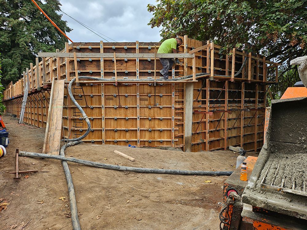 Construction site with wooden forms for a circular concrete structure; worker in green shirt, cement truck.