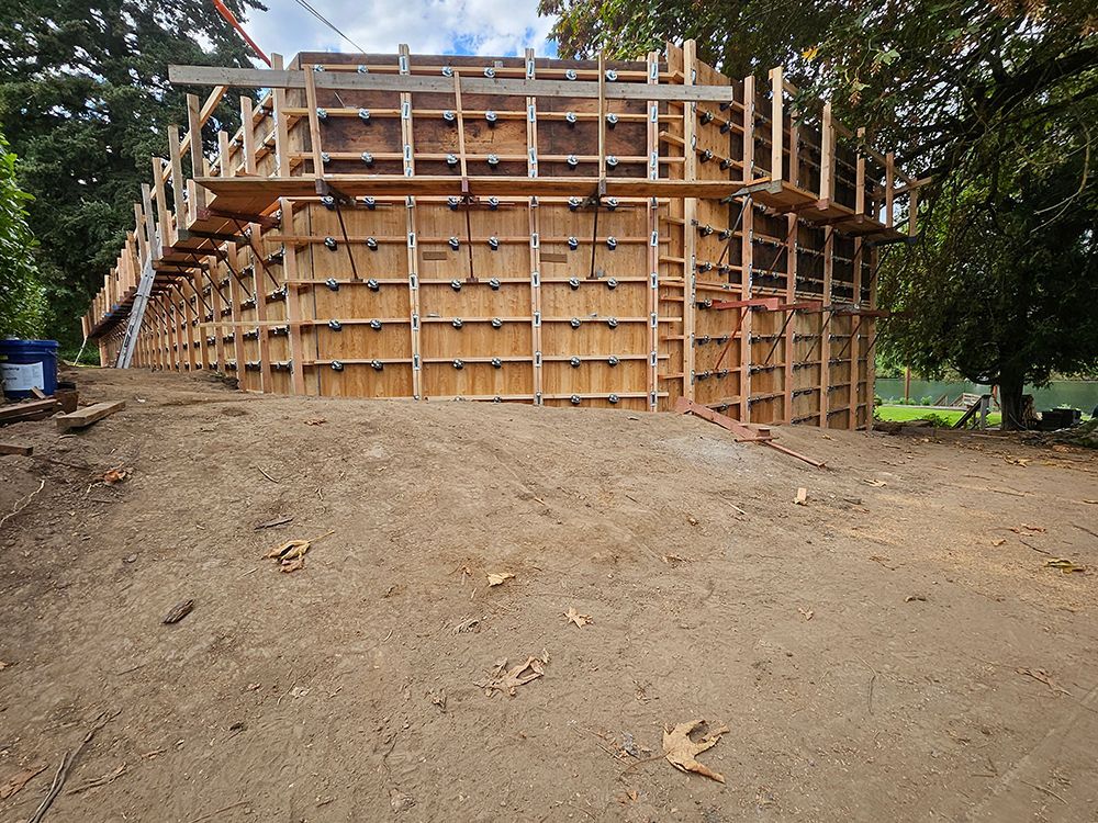 Wooden forms for a building under construction, set on a dirt slope, with trees in the background.