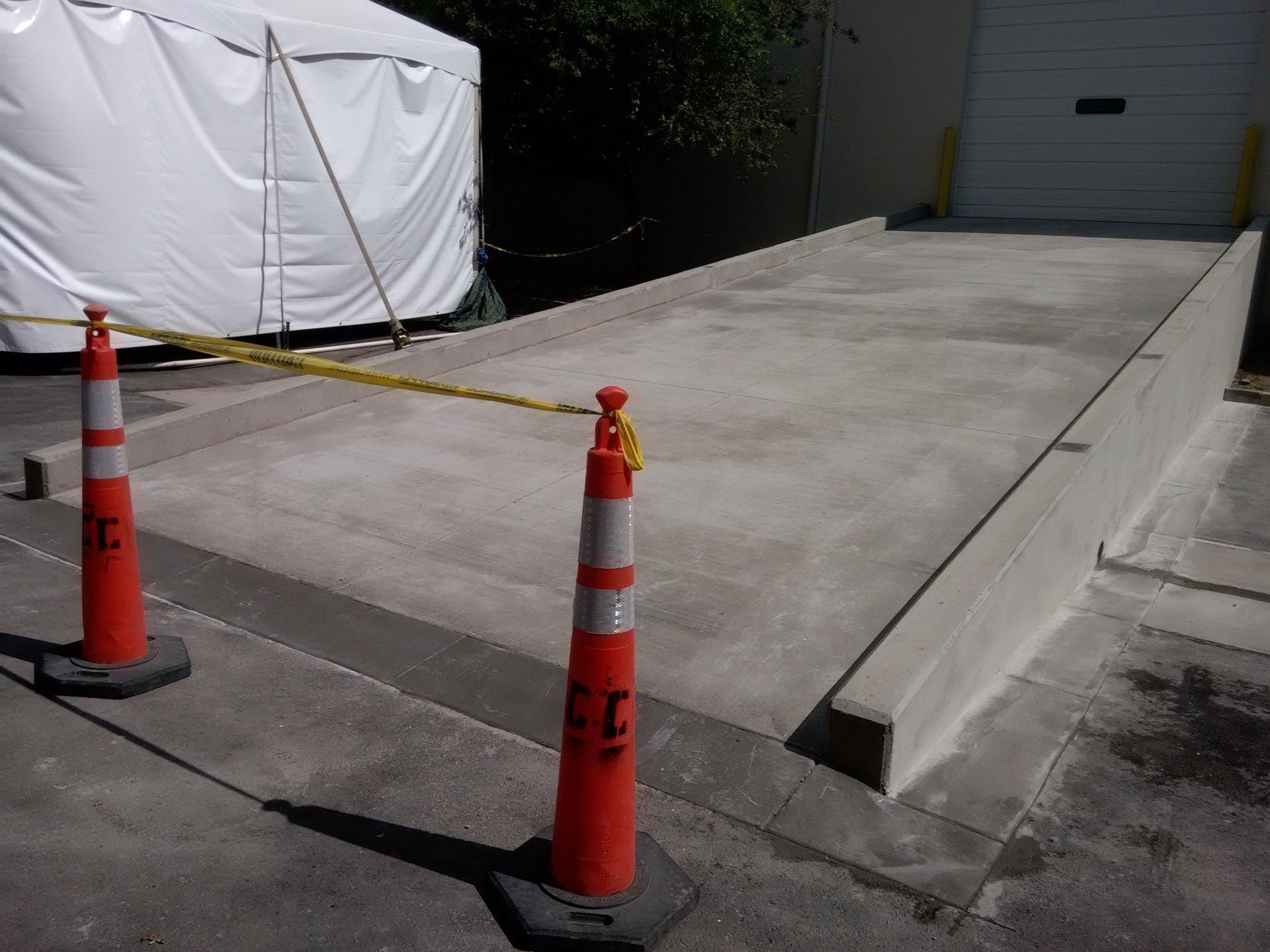 Concrete loading dock with caution tape and orange cones in front of a white tent.