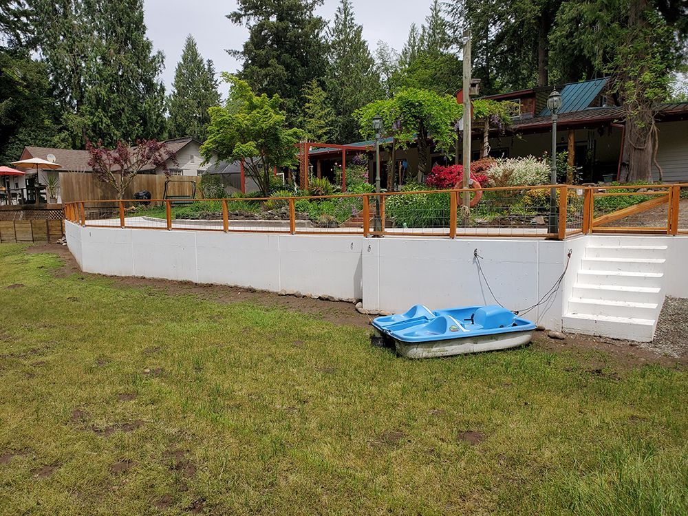 White retaining wall with wooden railing, steps, and a blue paddle boat on grass.