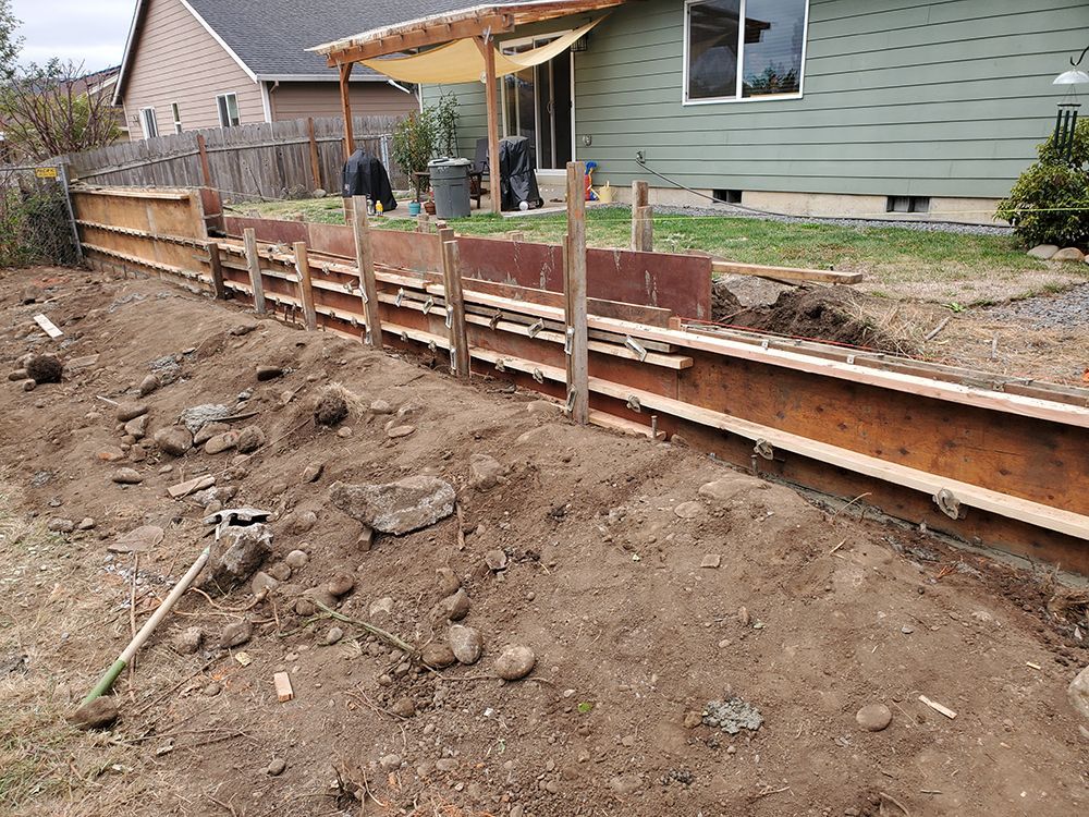 Construction site with a partially built fence and retaining wall in a backyard. Earth and wood are prominent.