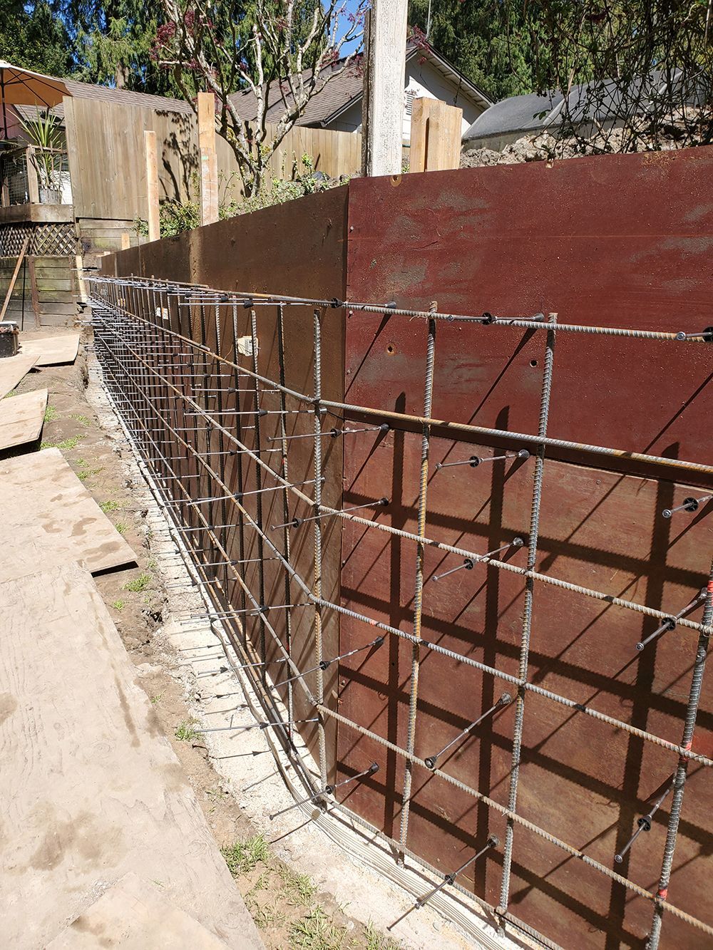 Steel reinforcing bars form a grid against a red-brown wall, possibly for a retaining wall construction.