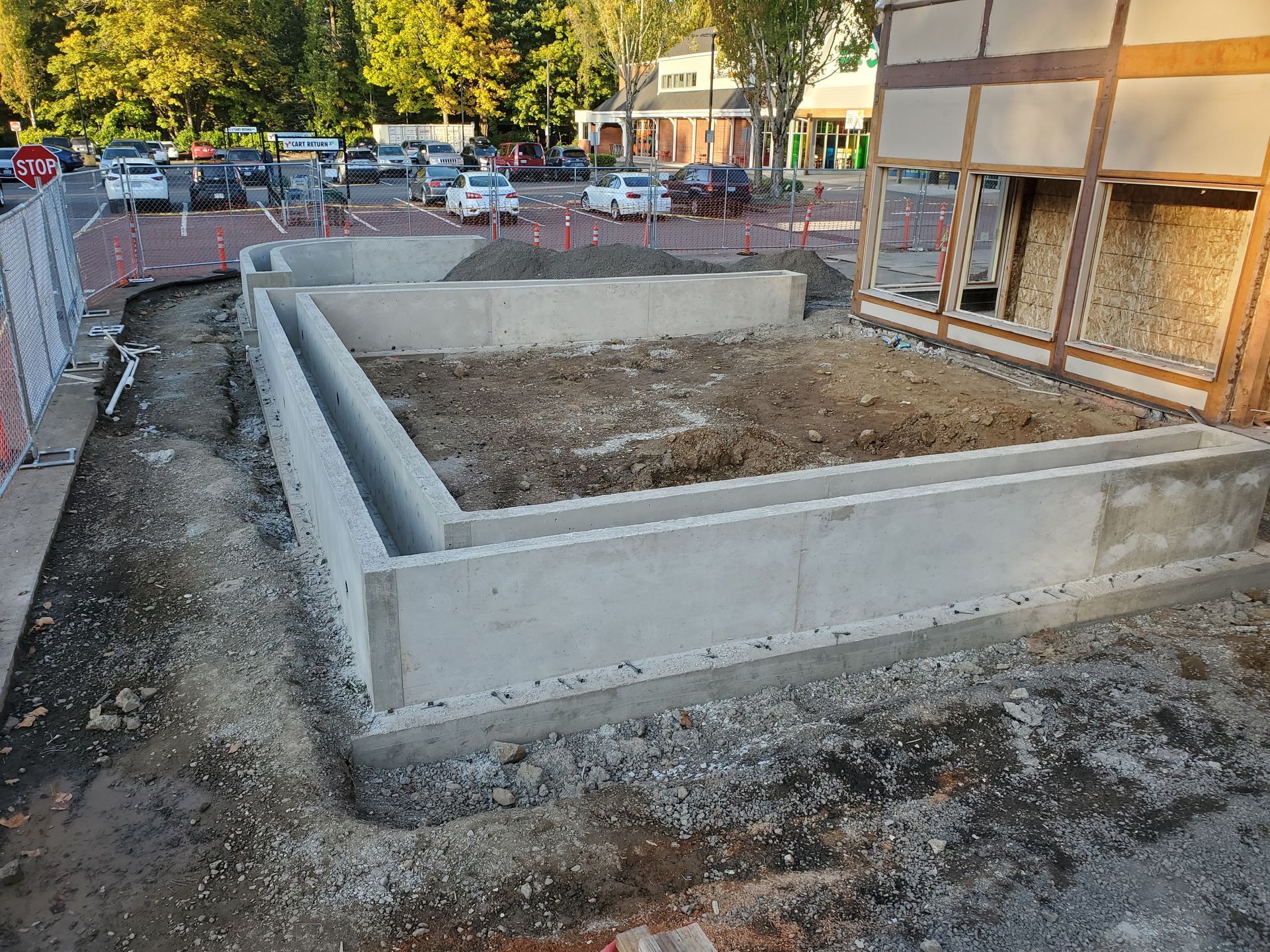 Concrete foundation of a building under construction, with exposed framing on the right side. Parking lot in the background.