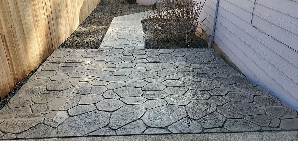 Stone patio with walkway leading to a house. Wooden fence on the left side.