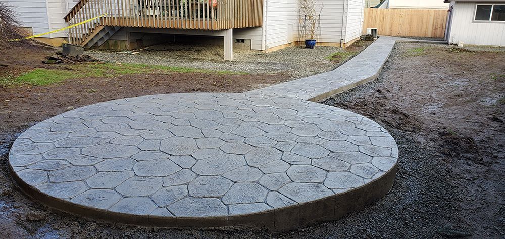Circular concrete patio with a walkway in a backyard.