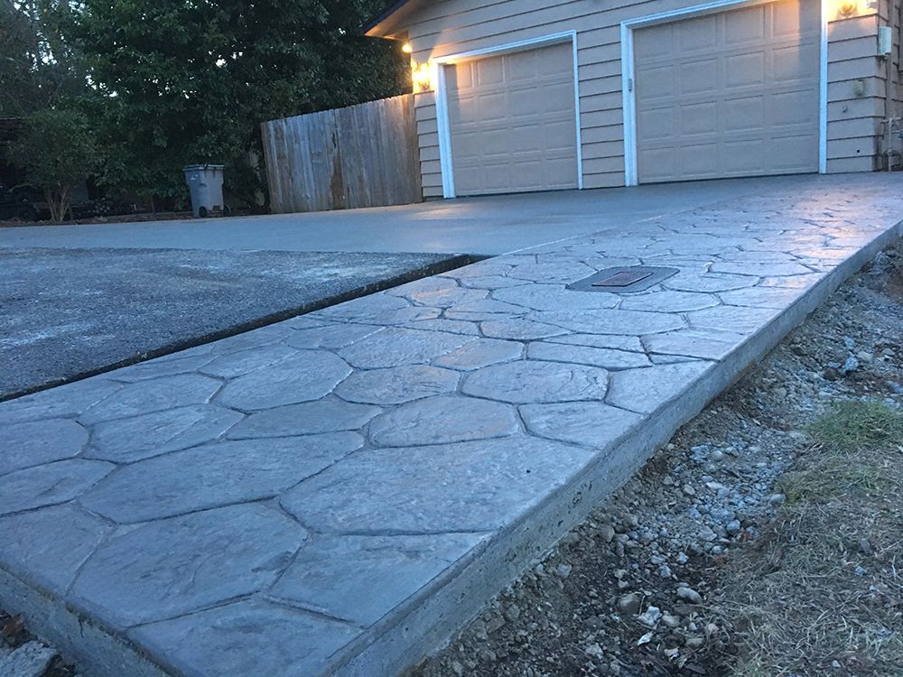 Concrete driveway and walkway with a patterned surface leading to a garage.