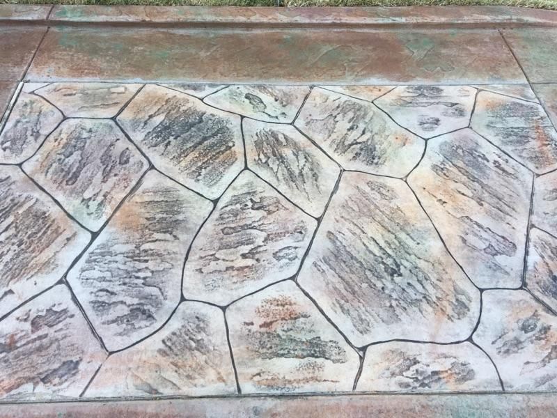 Stained concrete sidewalk with a textured, stone-like pattern in brown, gray, and green hues.