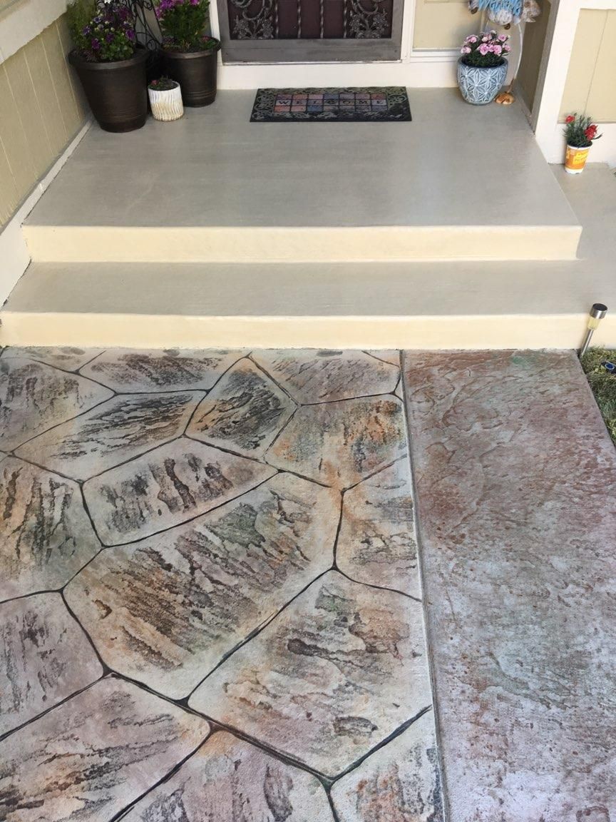 Stamped concrete walkway leading to a house entrance with steps. Stone pattern in earth tones.