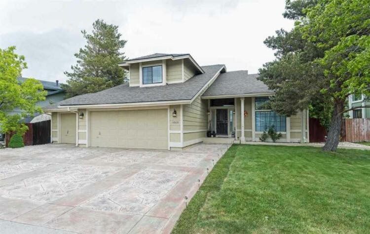House with beige siding, two-car garage, and a green lawn. Cloudy sky overhead.