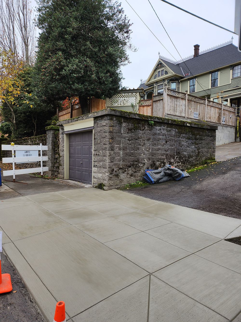 Concrete driveway leading to a stone garage and wooden fence; a house is in the background.
