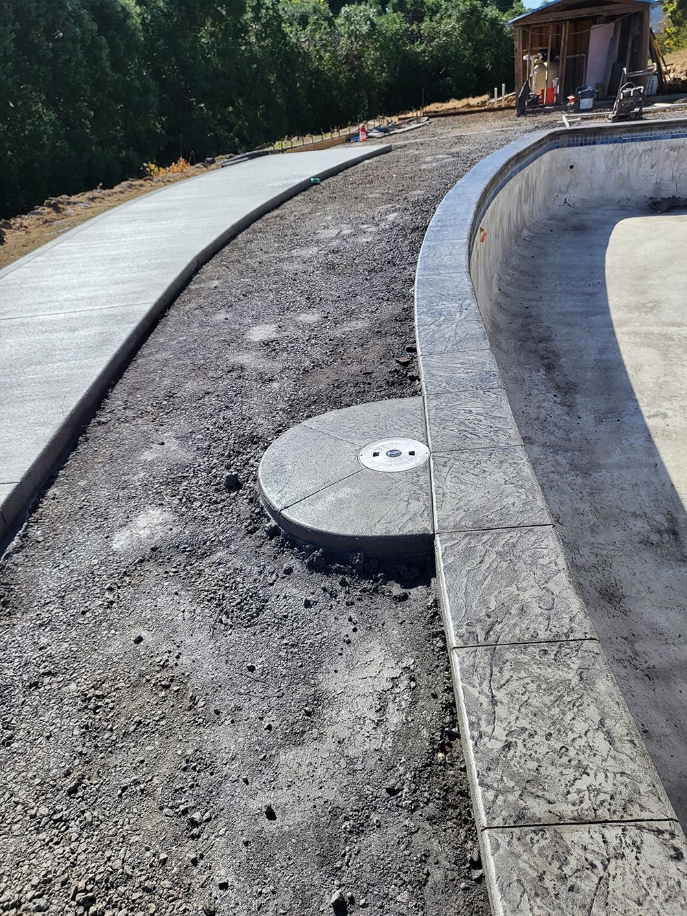 Concrete pathway and pool construction site with gravel ground.
