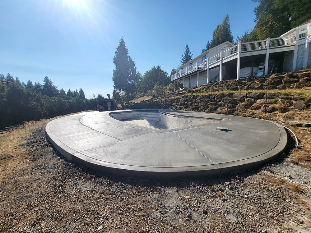 Circular concrete foundation with curved insets, near a house on a hillside.