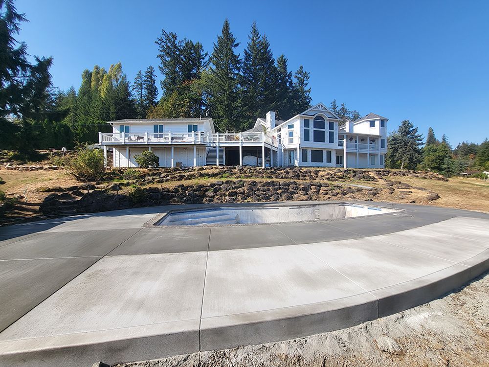 Large white house with deck overlooking newly poured concrete patio and pool area, sunny day.
