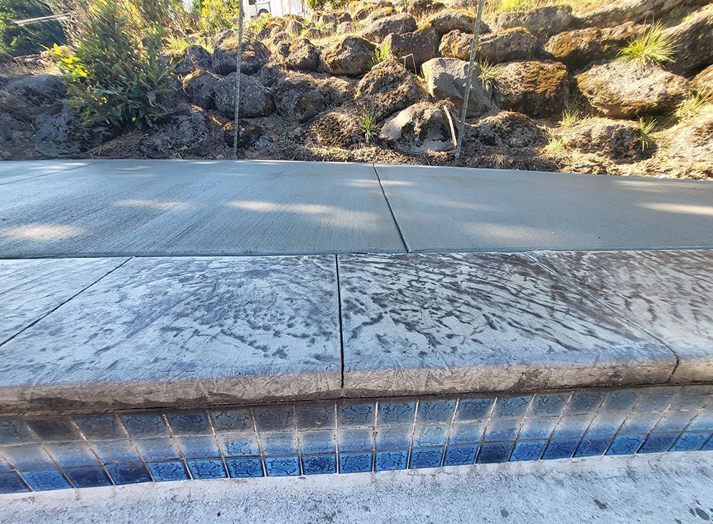 Concrete steps and walkway in front of a rock retaining wall, with blue tiles at the step's edge.